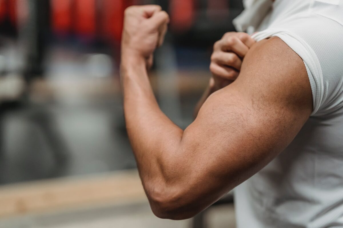 unrecognizable sportsman showing bicep in gym. One reason to eat to lose and gain muscles